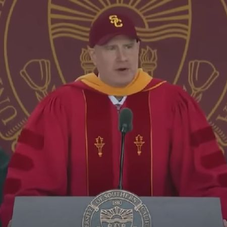 Kevin Feige is taking through a podium wearing a red gown.